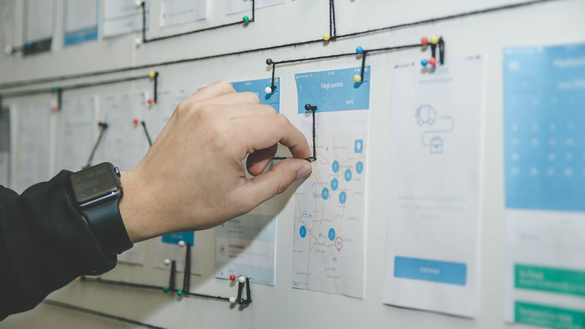 A hand sketching on wireframe cards pinned to a wall
